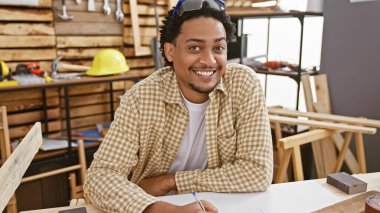 Marangozluk atölyesine gülümseyen kıvırcık saçlı yakışıklı adam mesleğini ve yaratıcılığını yansıtıyor..