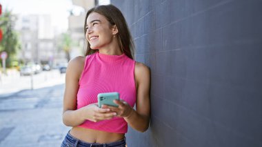 Tebessüm eden genç İspanyol kadın hareketli bir şehir caddesinde telefonuyla mesajlaşıyor. Mutluluk ve neşe saçıyor.