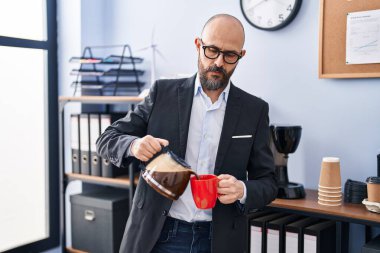 Genç kel iş adamı ofisteki bardağa kahve dolduruyor.