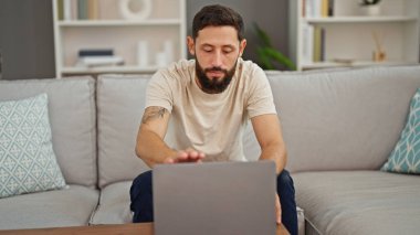 Genç İspanyol adam evdeki koltukta dizüstü bilgisayar kullanıyor.