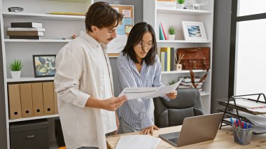 Erkek ve kadın, profesyonel takım çalışmasının bir örneği olarak modern ofis ortamında belgeleri gözden geçiriyorlar..