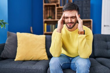 Young hispanic man stressed sitting on sofa at home