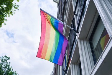 Canlı bir gökkuşağı bayrağı, beyaz bir binanın ön cephesinde gururla sergileniyor. Şehir ortamında Igbt 'ın gurur ve çeşitliliğini simgeliyor..