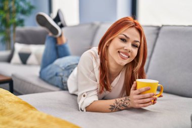 Kafkasyalı genç bir kadın evdeki kanepede kahve içiyor.