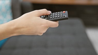 Kapalı bir evde, siyah bir televizyonun uzaktan kumandasını tutan birinin yakın çekimi..