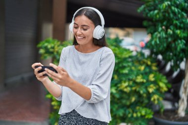 Genç ve güzel İspanyol kadın gülümsüyor. Sokakta akıllı telefondan videolar izliyor.