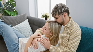 Sevecen bir adam, sıcak oturma odasında bir kadını başından öpüyor, sevgisini ve birlikteliğini ifade ediyor..