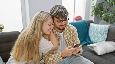 Sevgi dolu bir çift, rahat bir oturma odasında akıllı bir telefonla birlikte vakit geçirmekten zevk alır..