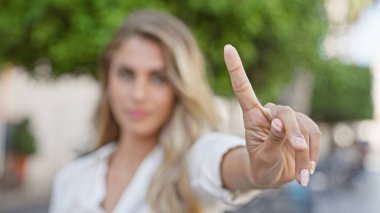 Serin, genç sarışın kadın rahat ama ciddi bir enerji yayıyor, güneşli, şehir sokağında dikiliyor, kamerayla göz teması kurarken kararlı bir şekilde hayır diyor.