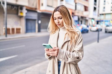 Sokakta akıllı telefon kullanan genç sarışın kadın.