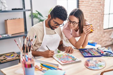 Man and woman artists drinking coffee drawing on notebook at art studio