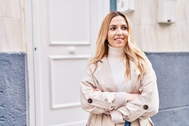 Sokakta kollarını kavuşturmuş genç sarışın kadın.