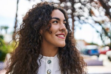 Genç, güzel, İspanyol bir kadın, gülümsüyor. Parkta kendine güveniyor.