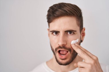 Sakallı İspanyol bir adam nemlendirici krem kullanıyor. Şaşırmış ve şaşırmış bir ifade, korku ve heyecanlı bir yüz ifadesi var.. 