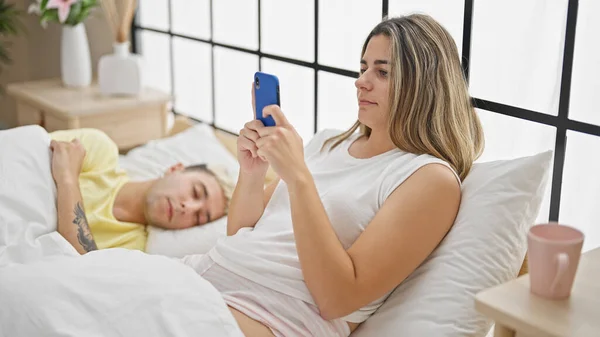 Beautiful couple lying on bed using smartphone while boyfriend sleep at bedroom
