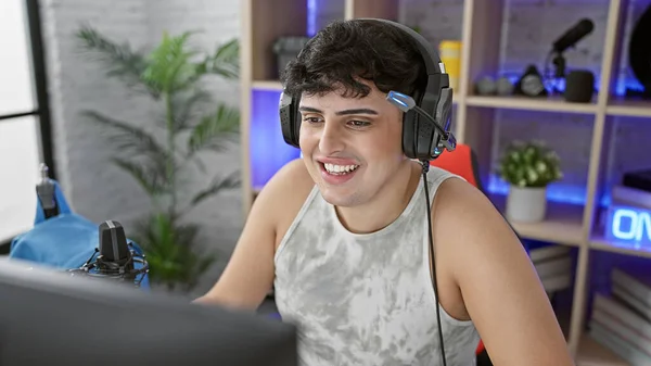 A happy young man gaming at home in a well-lit room with microphones and a headset, embodying a relaxed and fun atmosphere.