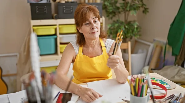 Mujer Artista Mediana Edad Delantal Amarillo Contemplando Pinceles Estudio Arte — Foto de Stock