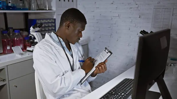 African american male scientist taking notes in a laboratory setting, surrounded by medical equipment.
