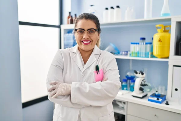 Young beautiful plus size woman scientist smiling confident standing with arms crossed gesture at pharmacy
