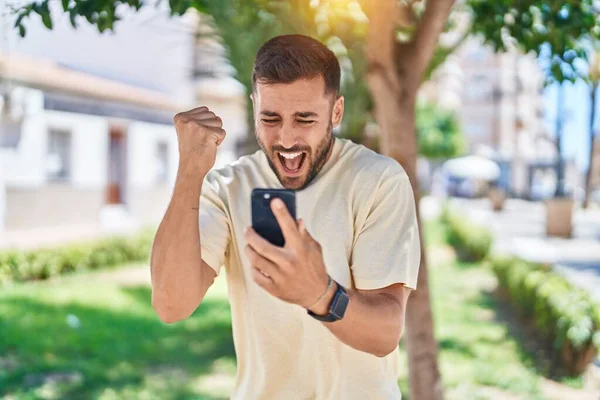 Νεαρός Ισπανόφωνος Χρησιμοποιώντας Smartphone Την Έκφραση Νικητής Στο Πάρκο — Φωτογραφία Αρχείου