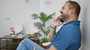 Beyaz duvarları olan modern bir bekleme odasında gülümseyen adam güllerle dolu bir sehpa ve arka planda yeşil bir bitki..
