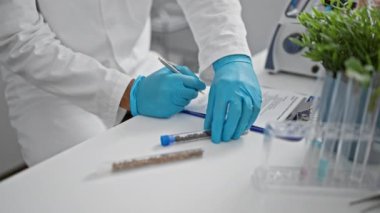 Laboratuvar önlüğü giymiş bir sağlık uzmanı test tüpleri ve modern bir laboratuvar ortamında santrifüj ile bir panoya yazı yazıyor..