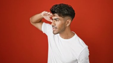 Sakallı neşeli İspanyol bir adam beyaz bir gömlek içinde canlı kırmızı bir arka plana karşı poz veriyor, kendine güven ve mutluluk yayıyor..