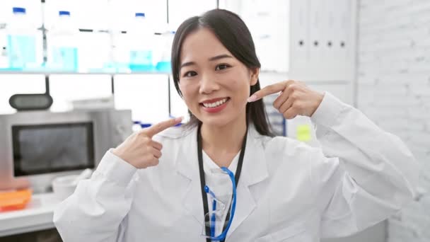 身穿白色实验室外套的快乐的中国年轻科学家指出了牙科保健问题 在实验室展示她灿烂牙齿的女人 促进健康的口腔护理 — 图库视频影像