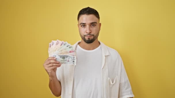 不幸な若いアラブ人男性は 黄色の背景に統一されたアラブ首長国連邦の紙幣と親指のサインを示し 拒絶と嫌悪のシンボル — ストック動画