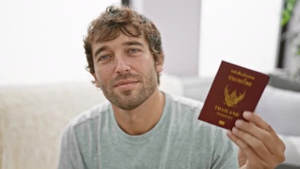 ジュビラントの若い男は喜んで快適なホームソファからタイのパスポートを点滅し 今後の冒険を予想する自信を除きます — ストック動画