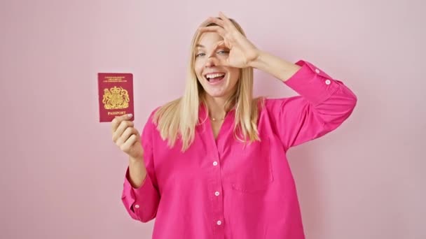 年轻快乐的金发女子用手捂住眼睛 闪烁着一个确定的标志 用她的手指在粉色孤立的背景下 用北部爱尔兰护照微笑着 — 图库视频影像