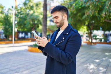 Genç İspanyol bir adam parkta akıllı telefon kullanıyor.