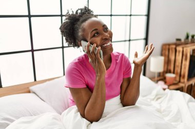 Afrika kökenli Amerikalı bir kadın akıllı telefondan konuşuyor. Yatak odasında oturuyor.