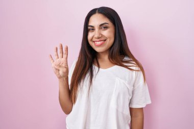 Pembe arka planda duran genç Arap kadın dört numarayı gösterip işaret ederken kendinden emin ve mutlu bir şekilde gülümsüyor.. 