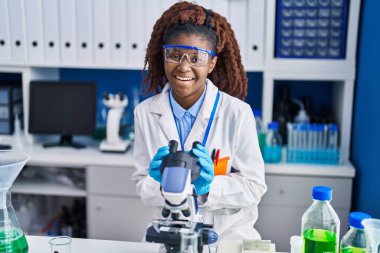 African american woman scientist smiling confident using microscope at laboratory
