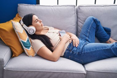 Genç, güzel İspanyol kadın evdeki kanepede müzik dinliyor.
