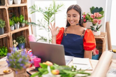Çiçekçide çalışan Latin asıllı genç bir kadın. Video çekiyor. Parmaklarıyla imza atıyor. 