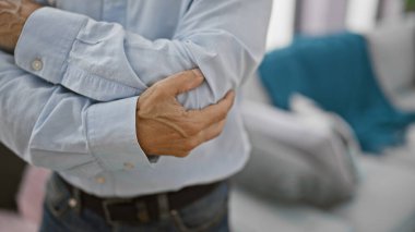 Yakışıklı, orta yaşlı, ispanyol, dirsek eklem ağrısı çeken bir adam. Oturma odasında duruyor. Yetişkin bir erkek, evinde kemik ağrısı çekiyor.