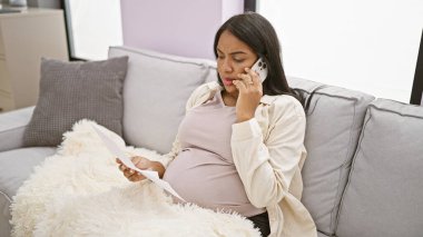 Evinin rahat köşelerinde, müstakbel genç bir kadın telefonda ciddi bir konuşma içinde, oturma odasındaki kanepede bir battaniyenin altına gizlenmiş, annelik belgelerini okuyor.