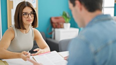 Ofisteki masada oturan iki işçi ve kadın evrak okuyorlar.