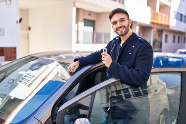 Young hispanic man smiling confident holding key of new car at street