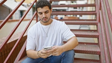 Şehir merdivenlerinde oturan genç adam akıllı telefon kullanarak çağdaş şehir yaşamını resmediyor..