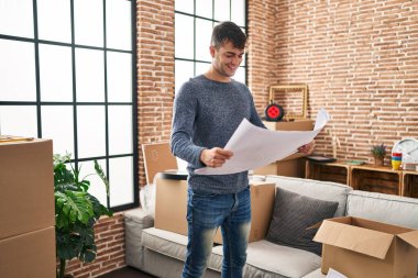 Genç İspanyol adam gülümsüyor. Kendine güvenen yeni ev planları okuyor.