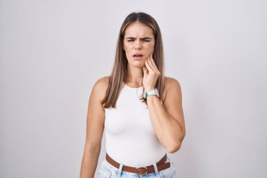 Beyaz arka planda duran Latin kökenli genç bir kadın diş ağrısı ya da diş ağrısı yüzünden elleriyle dudaklarına dokunuyor. dişçi 