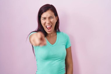 Young hispanic woman standing over pink background pointing displeased and frustrated to the camera, angry and furious with you 