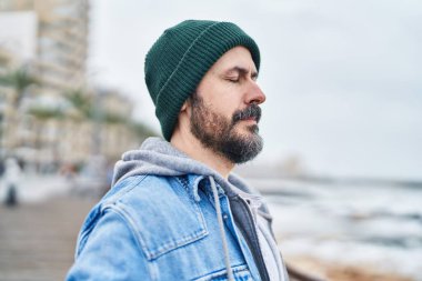 Genç kel adam deniz kenarında gözleri kapalı nefes alıyor.