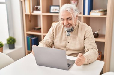 Middle age grey-haired man having video call sitting on table at home