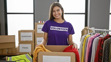 Kendine güveni tam genç İspanyol bir kadın, güzel gülümsüyor, hayır kurumunda kıyafet paketiyle gönüllü çalışıyor.