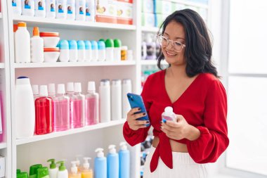 Genç Çinli kadın müşteri eczanede akıllı telefon kullanıyor.