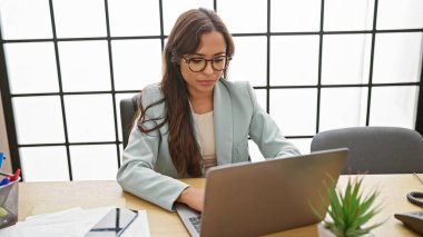 Ciddi ama rahat, odaklanmış genç bir İspanyol kadın zarif bir patron rolünü üstlenir. Güzel bir profesyonel. Ofis masasında dizüstü bilgisayarıyla özenle çalışıyor..